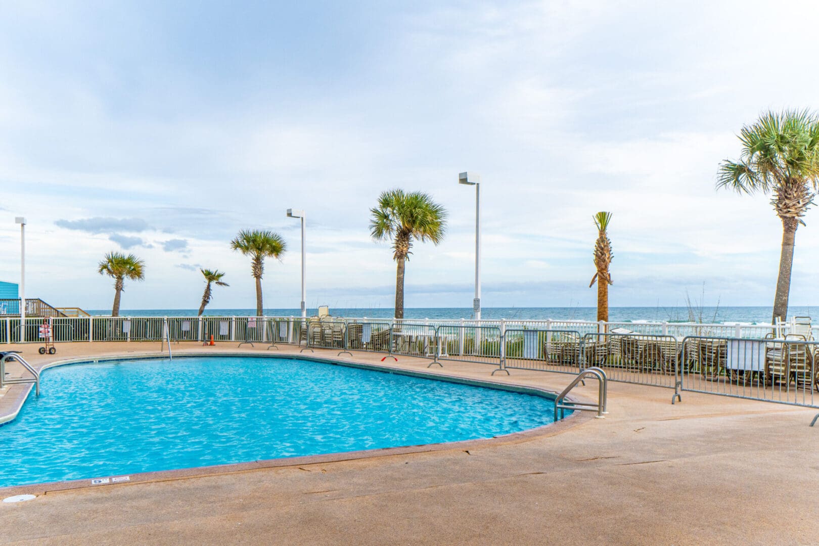 A pool with palm trees and the ocean in the background.