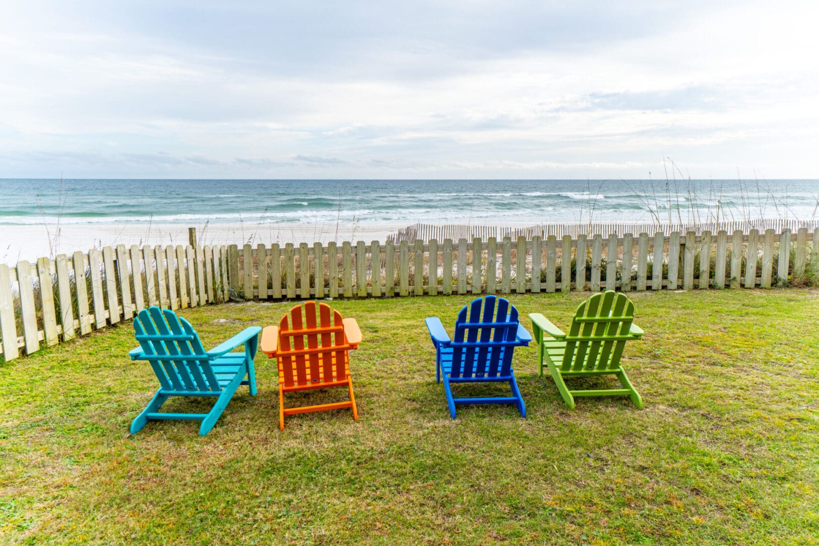 Four lawn chairs are sitting in a yard by the ocean.