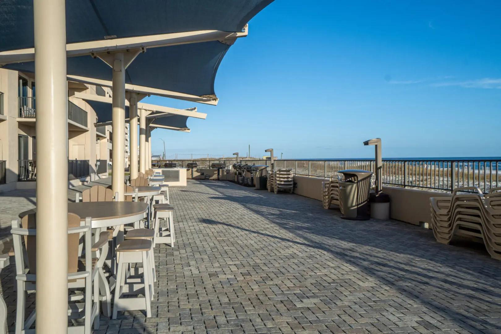 A patio with tables and chairs on the side of the beach.